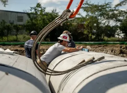 Construction site with excavators, concrete pipes, and trenches under a blue sky with clouds.